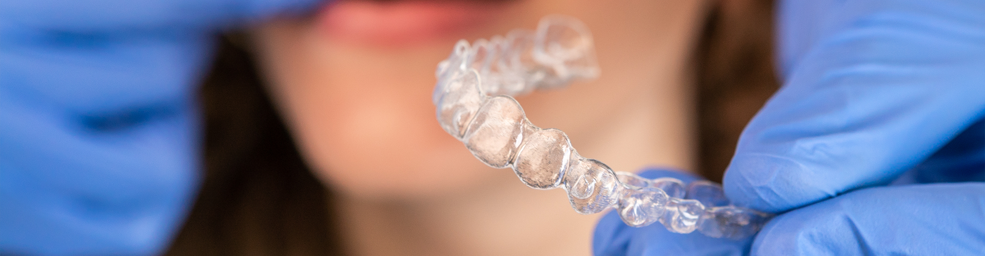 Gloved hands placing clear aligner in woman's mouth.